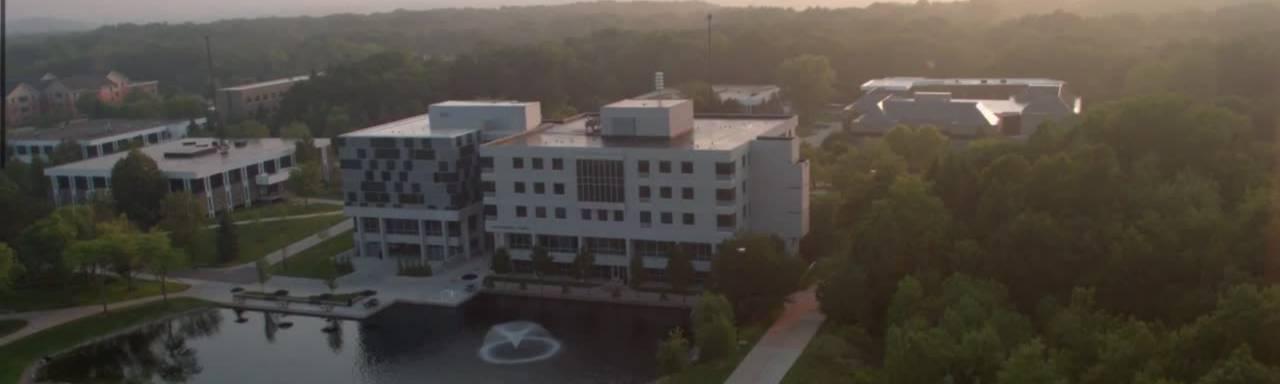 Aerial shot of a grey and blue square building near a small pond. Zumberge Hall on GVSU's Allendale Campus